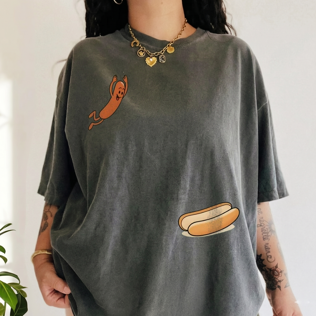 Person wearing an oversized dark grey graphic t-shirt featuring a cartoon hot dog diving into a bun on the front.