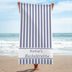 A woman holding a purple and white striped beach towel with custom name text on the sand.