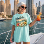 Woman wearing a mint green tropical beach graphic tee on a boat holding a cocktail, embracing the island vacation aesthetic.
