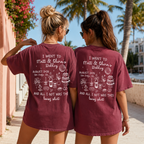 Two women wearing maroon t shirts with custom wedding text and souvenir table graphics on the back outdoors.