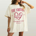 A woman wearing an oversized ivory graphic tee with red Newlyweds Club design, getaway car, and custom surname.