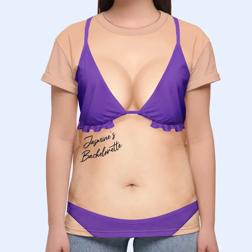 A woman models a purple bikini body bachelorette t-shirt featuring a realistic swimsuit print and custom script against a