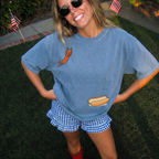 Smiling woman wearing a light blue hot dog oversized graphic t-shirt outdoors with US flags.