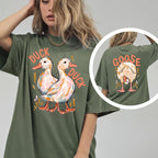 A woman wearing an olive green oversized t-shirt with a duck duck print on front and goose print on back.