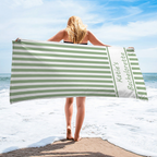A woman holding a green and white striped beach towel with custom name text at the seaside.
