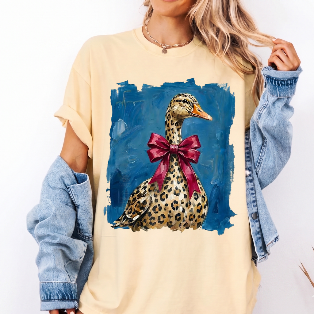 Butter-yellow Leopard Duck With Red Bow Graphic Tee worn with denim jacket in close-up front view.