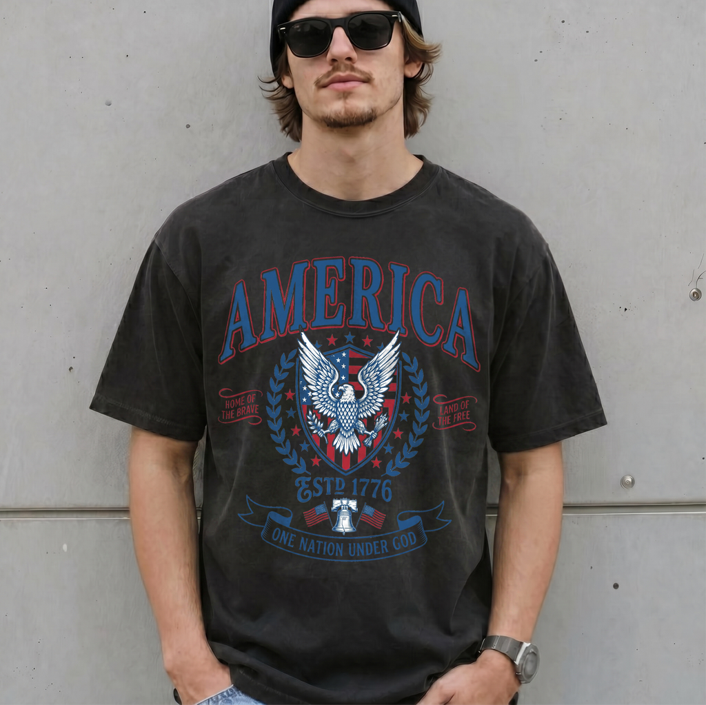 Man wearing a dark grey vintage America patriotic eagle graphic tee with sunglasses in front of a concrete wall