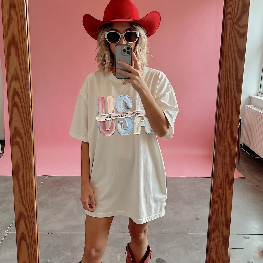 A woman in a white graphic tee and red cowboy hat posing in front of a pink backdrop.