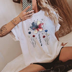 Woman holding a patterned phone wearing a white Comfort Colors T-Shirt with an American floral graphic tee design.