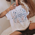Seated woman wearing white cotton graphic t-shirt with patriotic summer doodle print and black shorts.