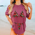 Woman wearing dark mauve graphic tee with leopard bikini graphic and red lips at the coast.