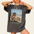 Woman wearing a charcoal grey Pregnant Girl Summer Graphic T-Shirt featuring a funny goldendoodle meme relaxing on the beach.