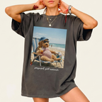 Woman wearing a charcoal grey Pregnant Girl Summer Graphic T-Shirt featuring a funny goldendoodle meme relaxing on the beach.