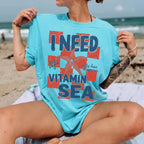 A woman relaxes on a beach towel in a bright blue graphic t-shirt featuring a starfish design and text.