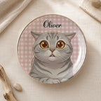 Round ceramic cat ring dish with custom name Oliver on a pink gingham background, displayed on neutral fabric.