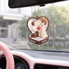 Custom engagement ornament hanging from a car mirror with a pink steering wheel and a blurred residential street outside.