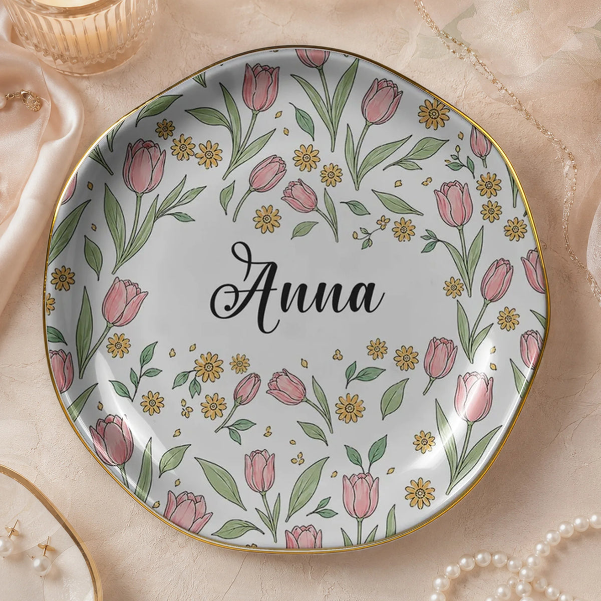 Round floral ceramic trinket dish on textured background featuring pink tulips, green leaves, gold rim, and the name Anna.