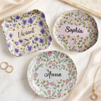 Three custom name jewelry trays in round, square, and wavy shapes featuring botanical floral designs and gold rims.