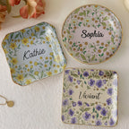 Three ceramic trinket dishes with floral illustrations and personalized script names displayed on a white surface.