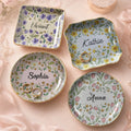 Four personalized floral ceramic trinket dishes in round, square, and wavy shapes with gold rims and custom names.