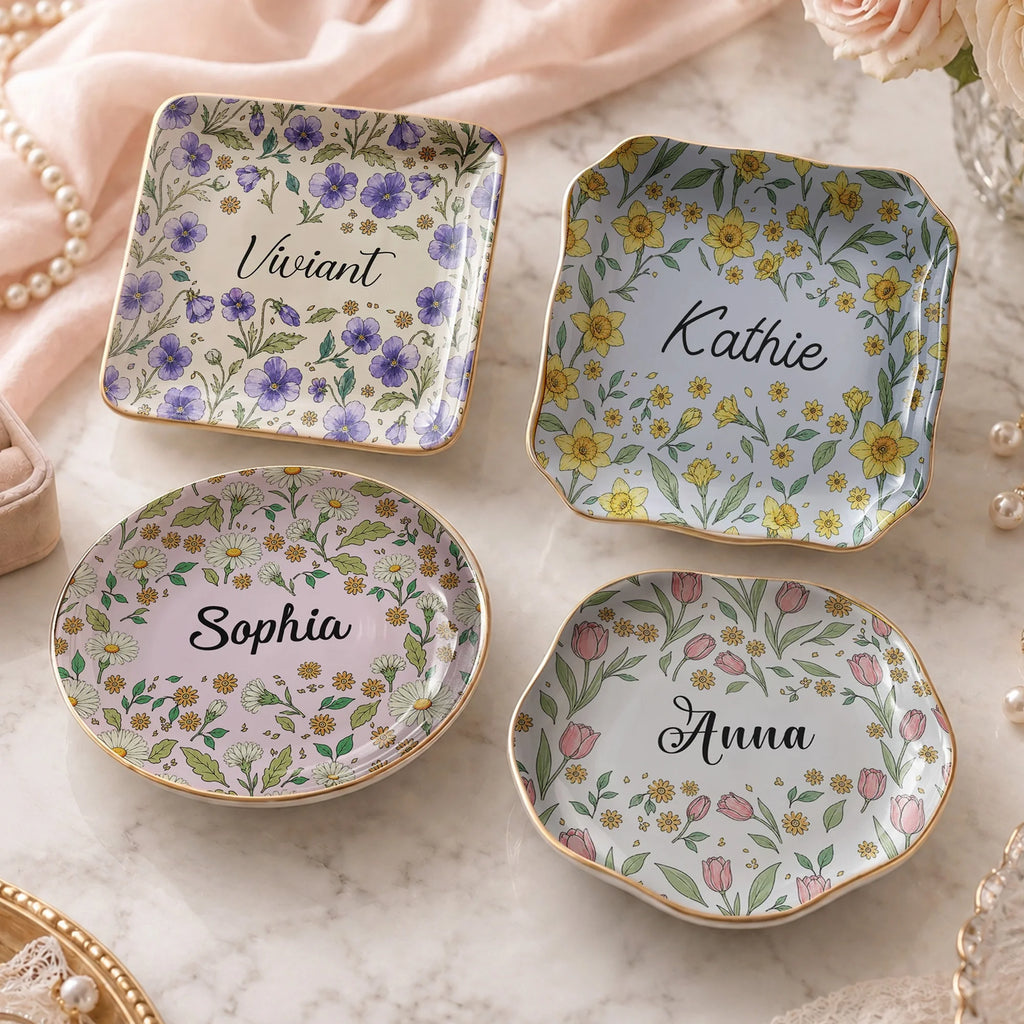 Four floral ceramic catchall dishes arranged on a pink surface with gold rims and custom names.