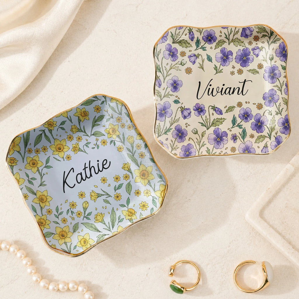 Two wavy square ceramic ring dishes with purple and yellow botanical birth flower prints and custom names.