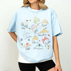 A woman in a light blue graphic t-shirt with watercolor princess tiaras and character signatures for theme parks.