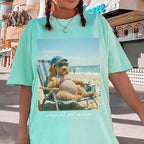 Mint green loose fit pregnancy top with a goldendoodle meme shirt graphic of a dog in a swimsuit on a beach lounger.