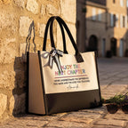 Next Chapter canvas tote bag with black and white ribbon bow standing beside a stone wall.