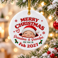 Personalized round ceramic ornament hanging on a Christmas tree, featuring a baby in a Santa hat and text 'Grandma & Grandpa