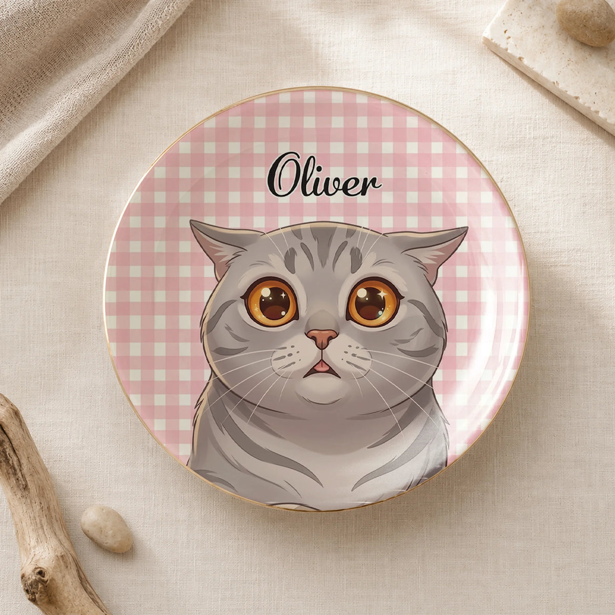 Round ceramic display plate with pink gingham background, gold rim, and an illustrated grey cat named Oliver.