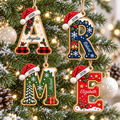 Four personalized wooden initial Christmas ornaments hanging on a snowy tree with lights.
