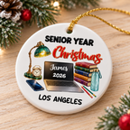 Round ceramic Senior Year Christmas ornament resting on a wooden surface with pine needles, personalized with James 2026.