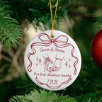 A round white ceramic ornament featuring a pinky promise hands graphic, names, and text hanging on a green pine tree branch.