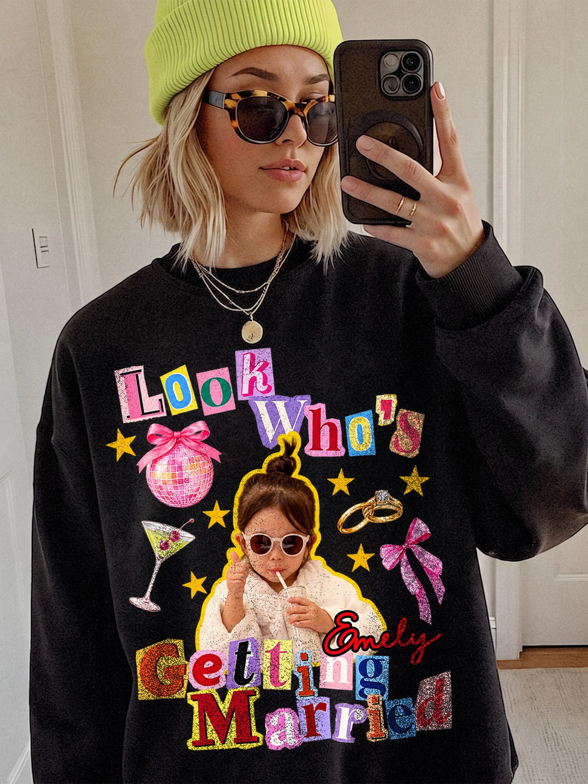A person wearing a black custom graphic sweatshirt and green beanie, showing a colorful retro collage design with a custom